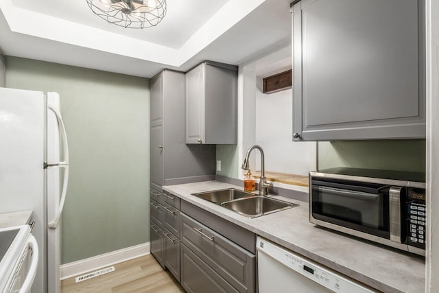 kitchen featuring sink, a tray ceiling, gray cabinets, white appliances, and light hardwood / wood-style floors