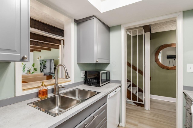 kitchen with sink, a skylight, white dishwasher, beamed ceiling, and light wood-type flooring