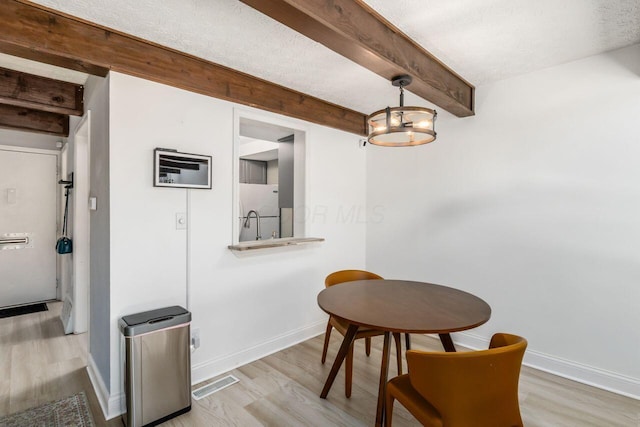 dining area with a textured ceiling, light hardwood / wood-style flooring, and beamed ceiling