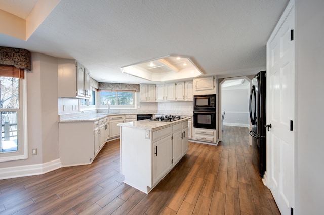 kitchen with a tray ceiling, black appliances, a center island, and white cabinets