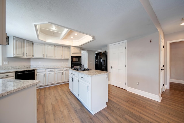 kitchen with a kitchen island, black appliances, white cabinetry, a tray ceiling, and light stone countertops