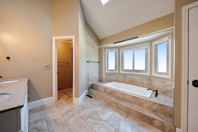 bathroom with plenty of natural light, tiled bath, vaulted ceiling with skylight, and vanity