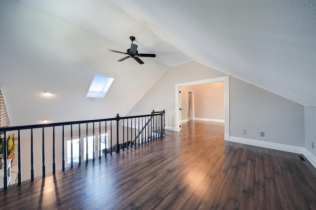 bonus room featuring lofted ceiling with skylight, dark wood-type flooring, a textured ceiling, and ceiling fan