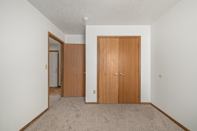 unfurnished bedroom with light carpet, a closet, and a textured ceiling