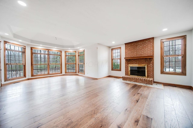 unfurnished living room with a tray ceiling, a fireplace, and light hardwood / wood-style flooring