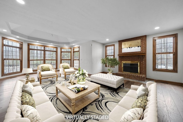 living room featuring a brick fireplace, a tray ceiling, and light wood-type flooring