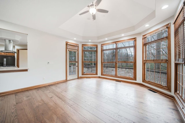 unfurnished room with a tray ceiling, light hardwood / wood-style floors, and ceiling fan