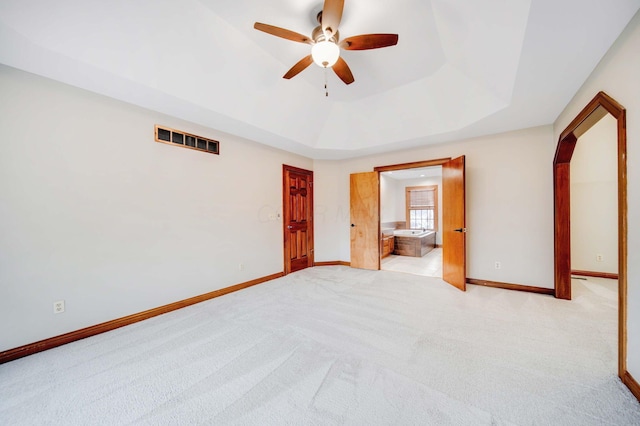 unfurnished bedroom with light carpet, connected bathroom, a tray ceiling, and ceiling fan