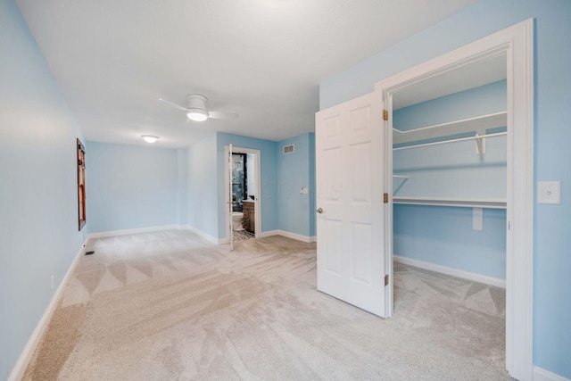 unfurnished bedroom with ceiling fan, ensuite bathroom, a walk in closet, light colored carpet, and a closet