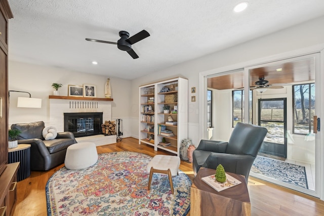 living room with ceiling fan, a fireplace, light hardwood / wood-style floors, and a textured ceiling