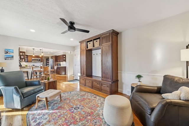 living room with ceiling fan, a textured ceiling, and light wood-type flooring