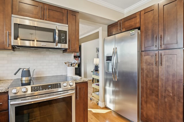 kitchen featuring light stone counters, light wood-type flooring, ornamental molding, appliances with stainless steel finishes, and decorative backsplash