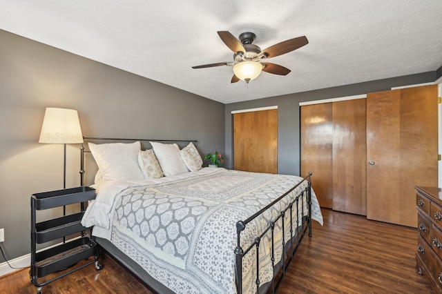 bedroom featuring dark wood-type flooring, ceiling fan, a textured ceiling, and two closets