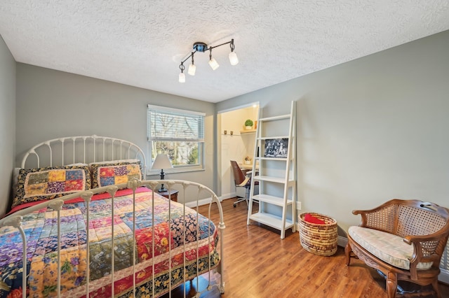 bedroom featuring wood-type flooring, rail lighting, and a textured ceiling