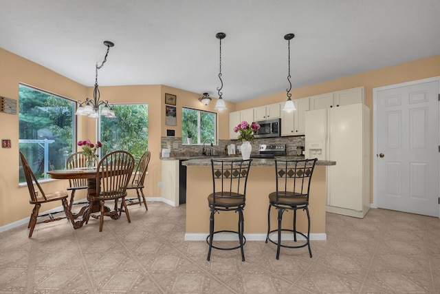 kitchen with a kitchen island, appliances with stainless steel finishes, stone countertops, decorative light fixtures, and white cabinets