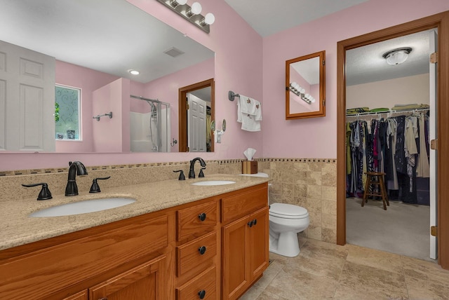 bathroom featuring vanity, toilet, a shower with door, and tile walls