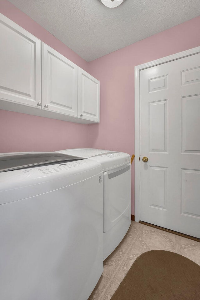 laundry room featuring cabinets, washing machine and clothes dryer, and a textured ceiling