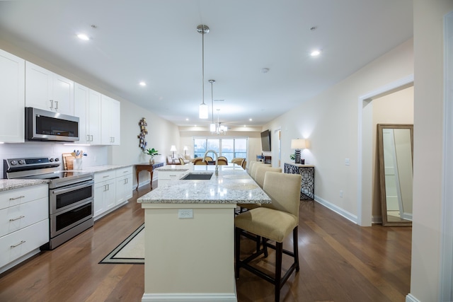 kitchen with a breakfast bar, sink, hanging light fixtures, appliances with stainless steel finishes, and an island with sink