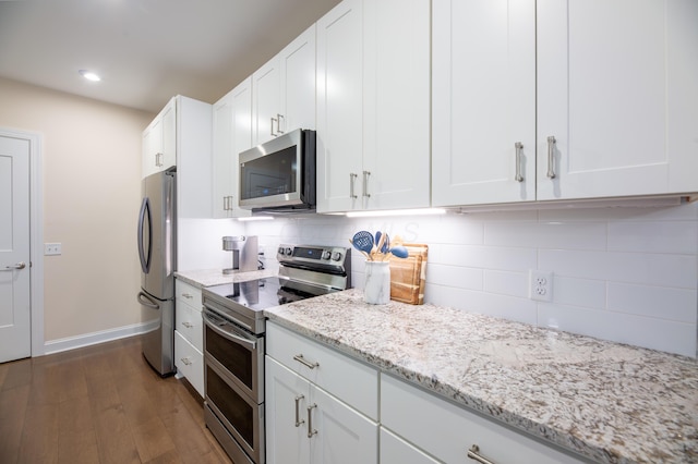 kitchen featuring dark wood-type flooring, white cabinetry, stainless steel appliances, light stone countertops, and decorative backsplash