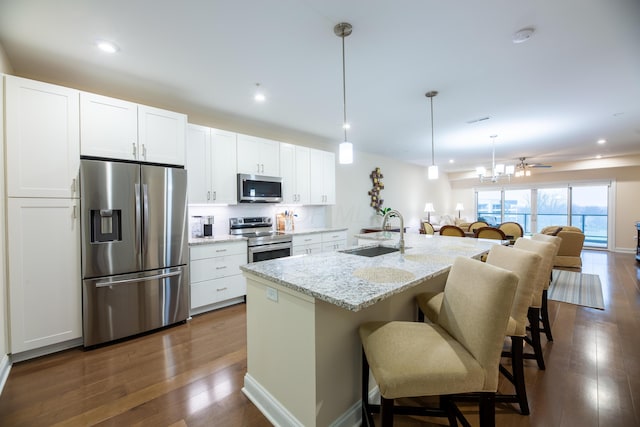 kitchen with sink, appliances with stainless steel finishes, hanging light fixtures, white cabinets, and a center island with sink