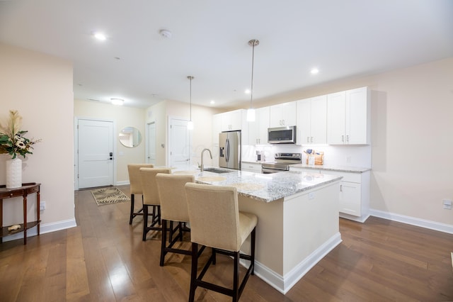 kitchen with sink, stainless steel appliances, light stone countertops, an island with sink, and white cabinets