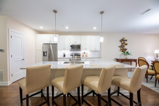 kitchen featuring sink, a breakfast bar, appliances with stainless steel finishes, an island with sink, and decorative light fixtures