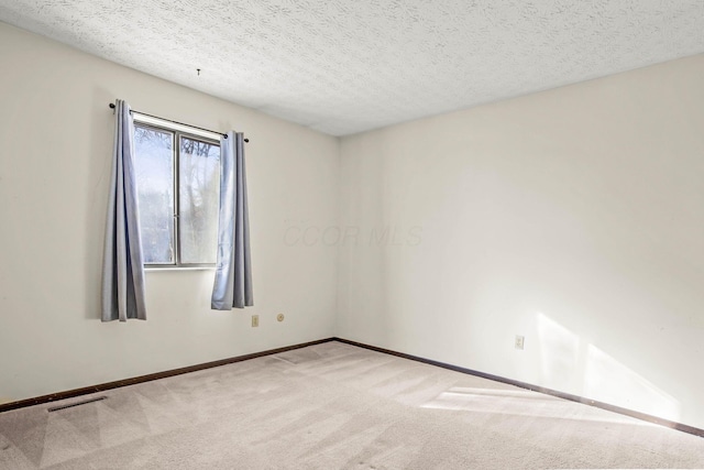 empty room with light colored carpet and a textured ceiling