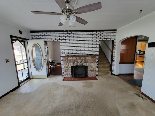 unfurnished living room featuring crown molding, a fireplace, ceiling fan, and brick wall