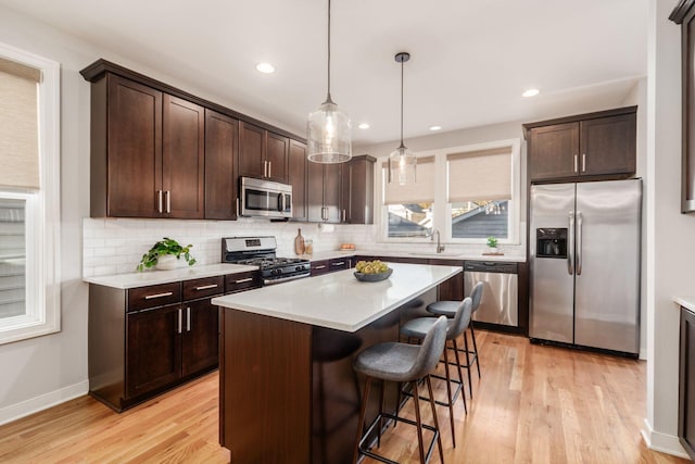 kitchen with decorative light fixtures, dark brown cabinets, light wood-type flooring, a kitchen island, and stainless steel appliances