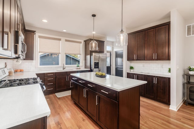 kitchen featuring appliances with stainless steel finishes, decorative light fixtures, sink, a center island, and light hardwood / wood-style floors