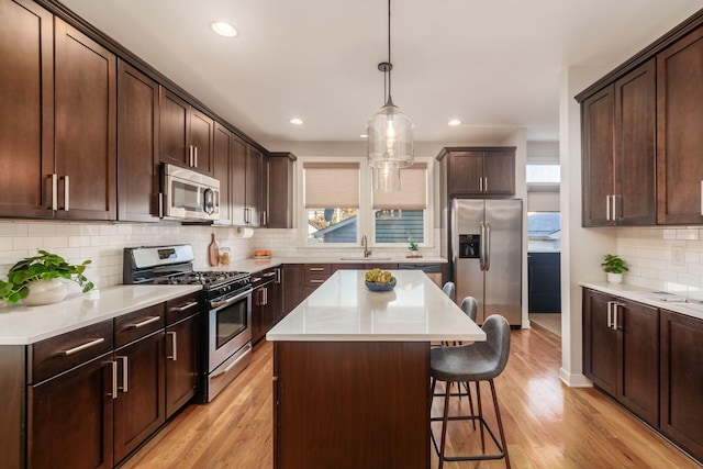 kitchen with appliances with stainless steel finishes, decorative backsplash, a center island, dark brown cabinets, and light wood-type flooring