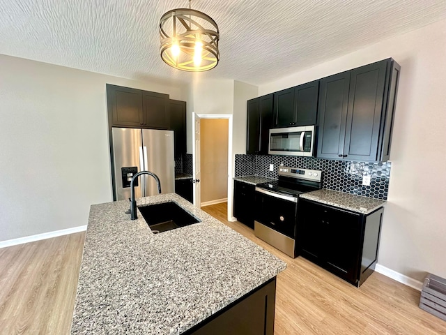 kitchen with light stone counters, sink, light wood-type flooring, and appliances with stainless steel finishes