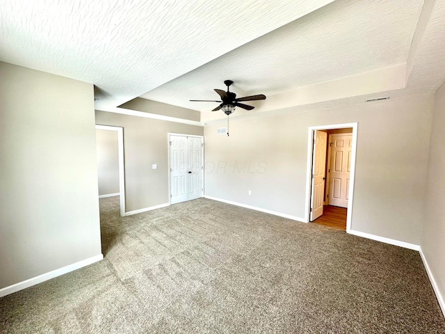 spare room with a tray ceiling, a textured ceiling, ceiling fan, and carpet flooring