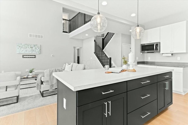 kitchen featuring a kitchen island, a towering ceiling, decorative light fixtures, white cabinetry, and light hardwood / wood-style flooring