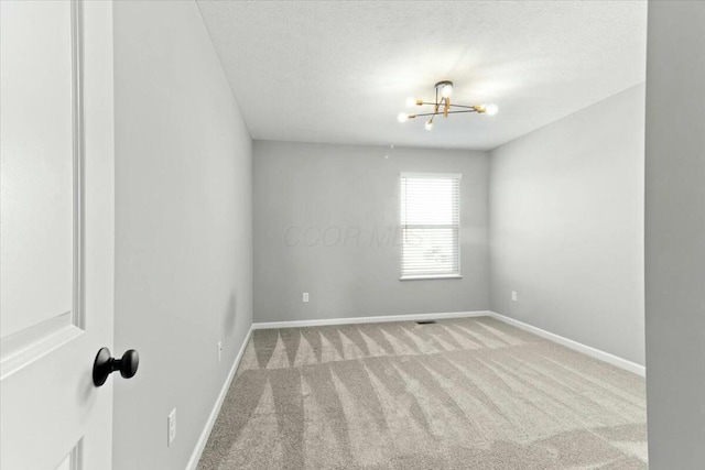 spare room featuring an inviting chandelier, light carpet, and a textured ceiling