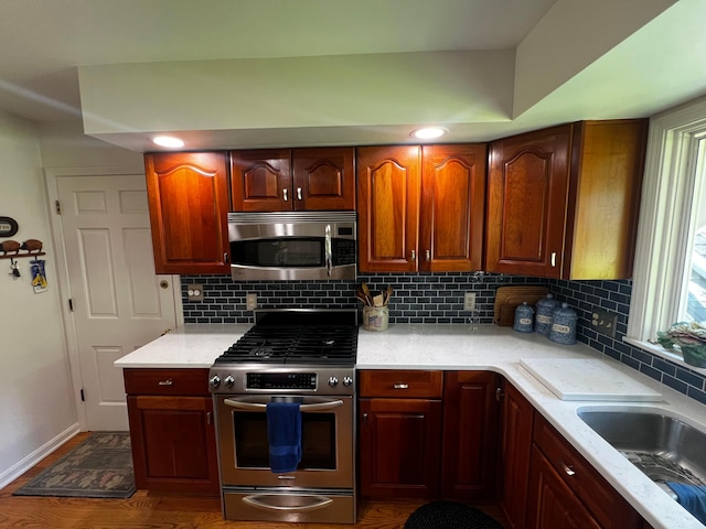 kitchen with appliances with stainless steel finishes, dark hardwood / wood-style floors, sink, decorative backsplash, and light stone counters