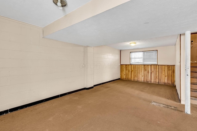 basement featuring light colored carpet, a textured ceiling, and wood walls