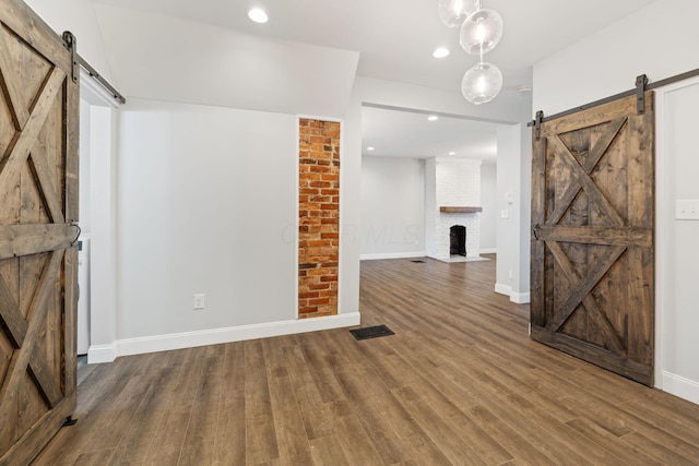 unfurnished living room with dark wood-type flooring, a fireplace, and a barn door