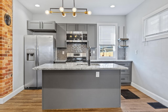 kitchen with gray cabinets, light stone countertops, an island with sink, and appliances with stainless steel finishes