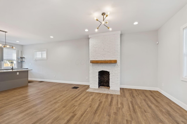 unfurnished living room with a brick fireplace, sink, and light wood-type flooring