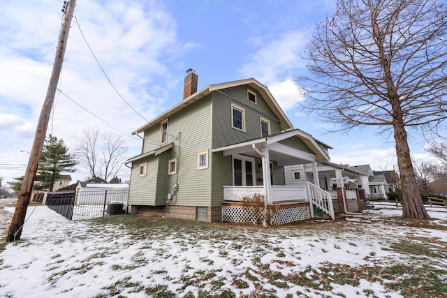 snow covered rear of property with a porch and central AC unit