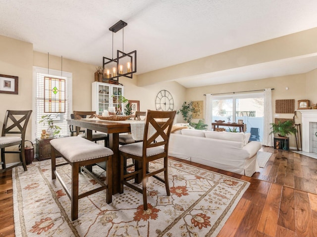 dining room featuring an inviting chandelier, hardwood / wood-style flooring, a tile fireplace, and a textured ceiling