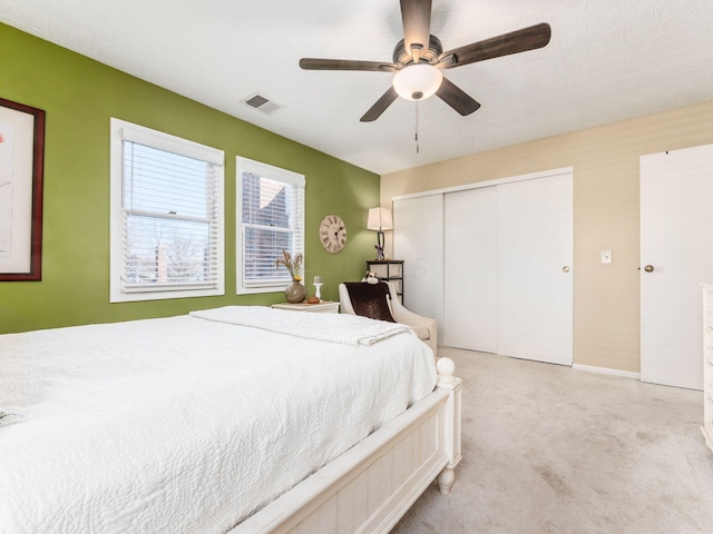 bedroom with ceiling fan, light carpet, a closet, and a textured ceiling