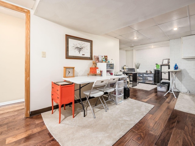 office with a paneled ceiling, dark hardwood / wood-style floors, and brick wall