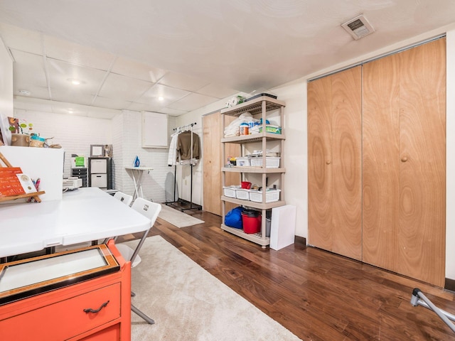 home office with dark wood-type flooring, a paneled ceiling, and brick wall