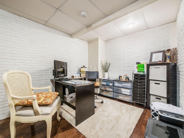 office area with brick wall, a paneled ceiling, and dark hardwood / wood-style flooring