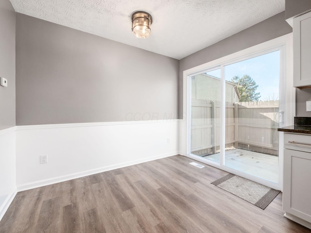 unfurnished dining area with a textured ceiling and light hardwood / wood-style flooring