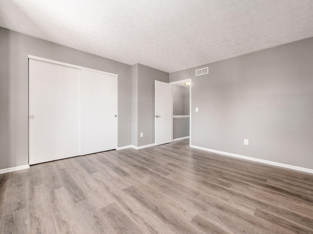 unfurnished bedroom with wood-type flooring, a closet, and a textured ceiling