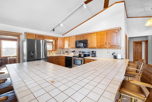 kitchen featuring a breakfast bar, tile counters, kitchen peninsula, and black appliances