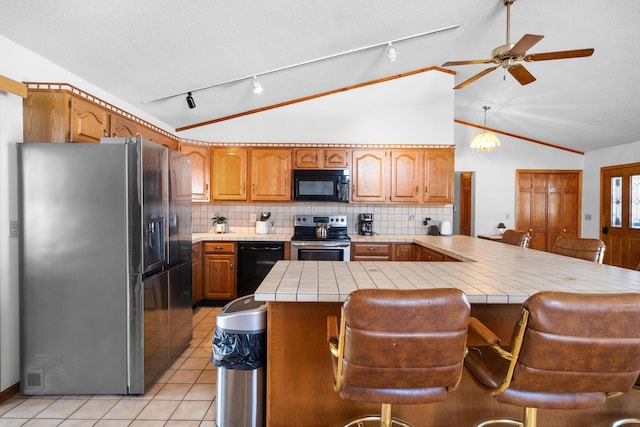 kitchen with appliances with stainless steel finishes, tile counters, a kitchen breakfast bar, and kitchen peninsula